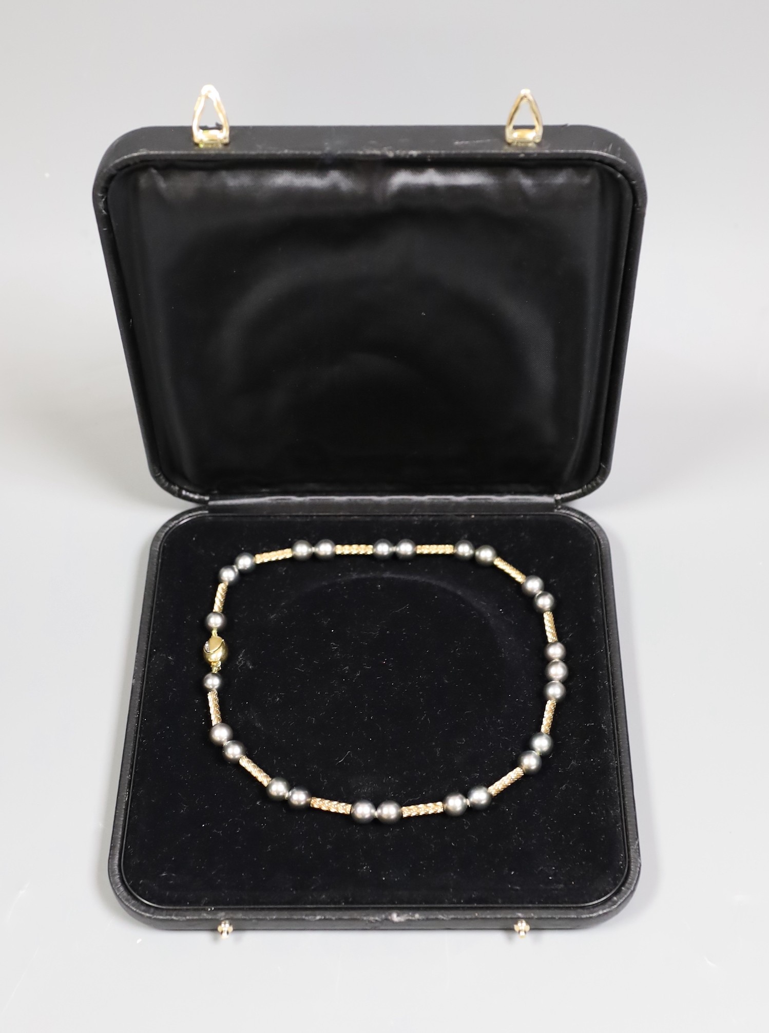 A cased modern 750 yellow metal and Tahitian? pearl set necklace, with diamond chip set clasp, 39cm, gross weight 31.1 grams.
